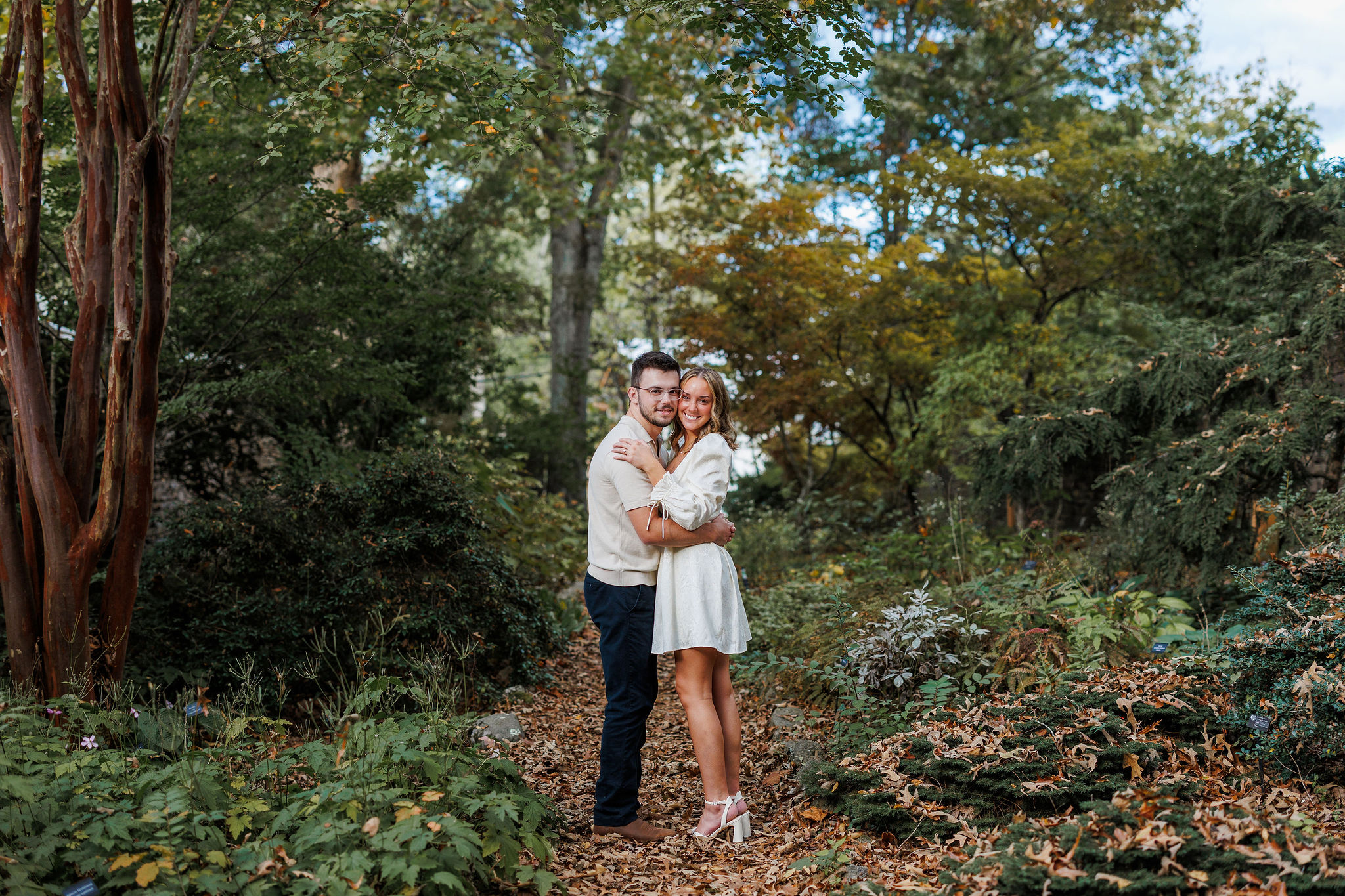 A couple wearing white embraces in a beautiful, green forest.